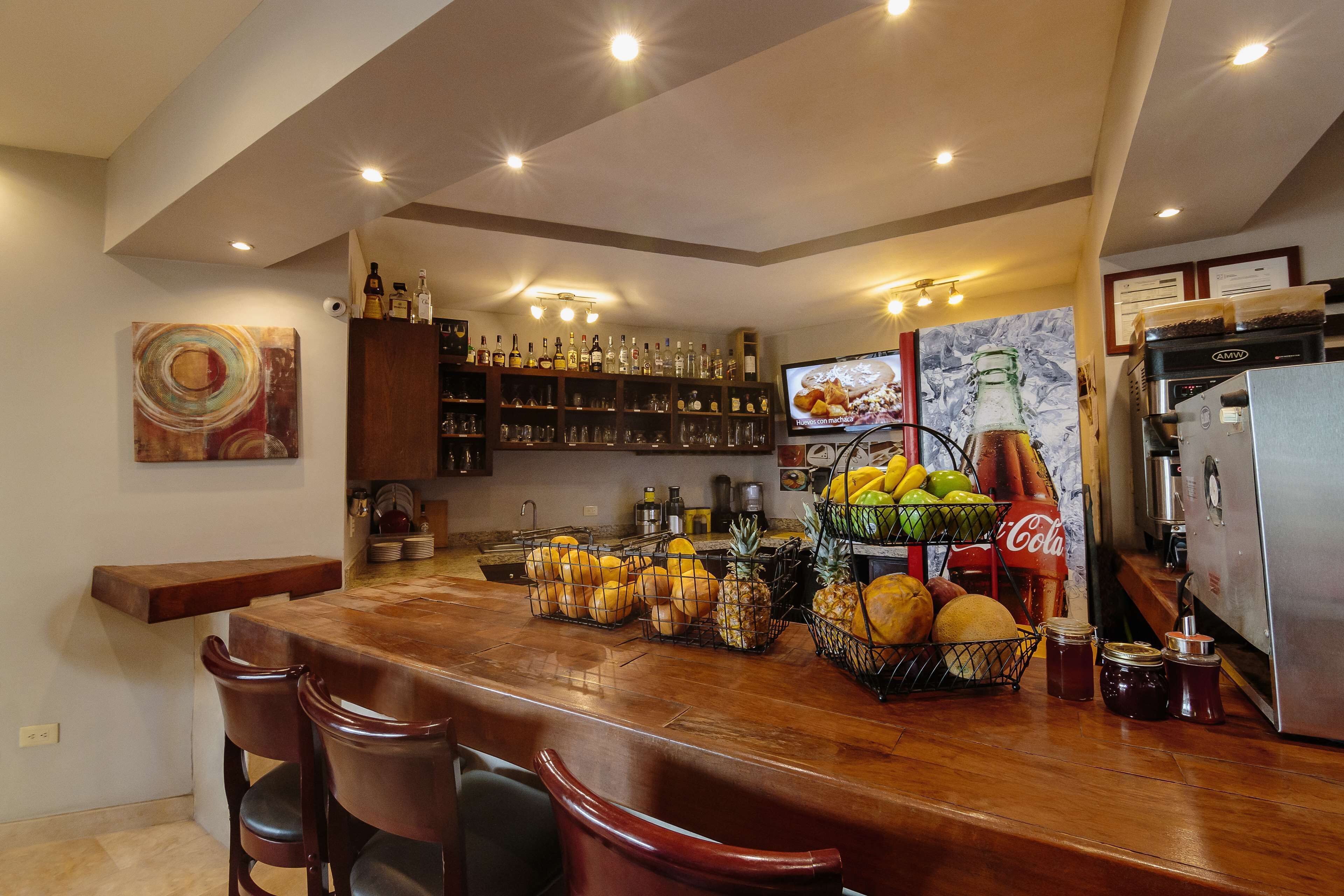 A kitchen with a wooden bar area, stocked with various bottles and a fruit basket.