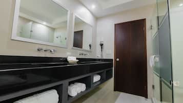 A modern bathroom with a black vanity, two large mirrors, a glass shower enclosure, and a wooden door.
