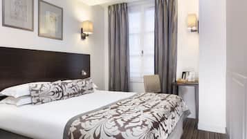 A hotel room with a large bed, a desk with a chair, and a window with curtains.
