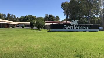 A sign for 'Settlement' with a palm tree logo, surrounded by a grassy area and buildings in the background.