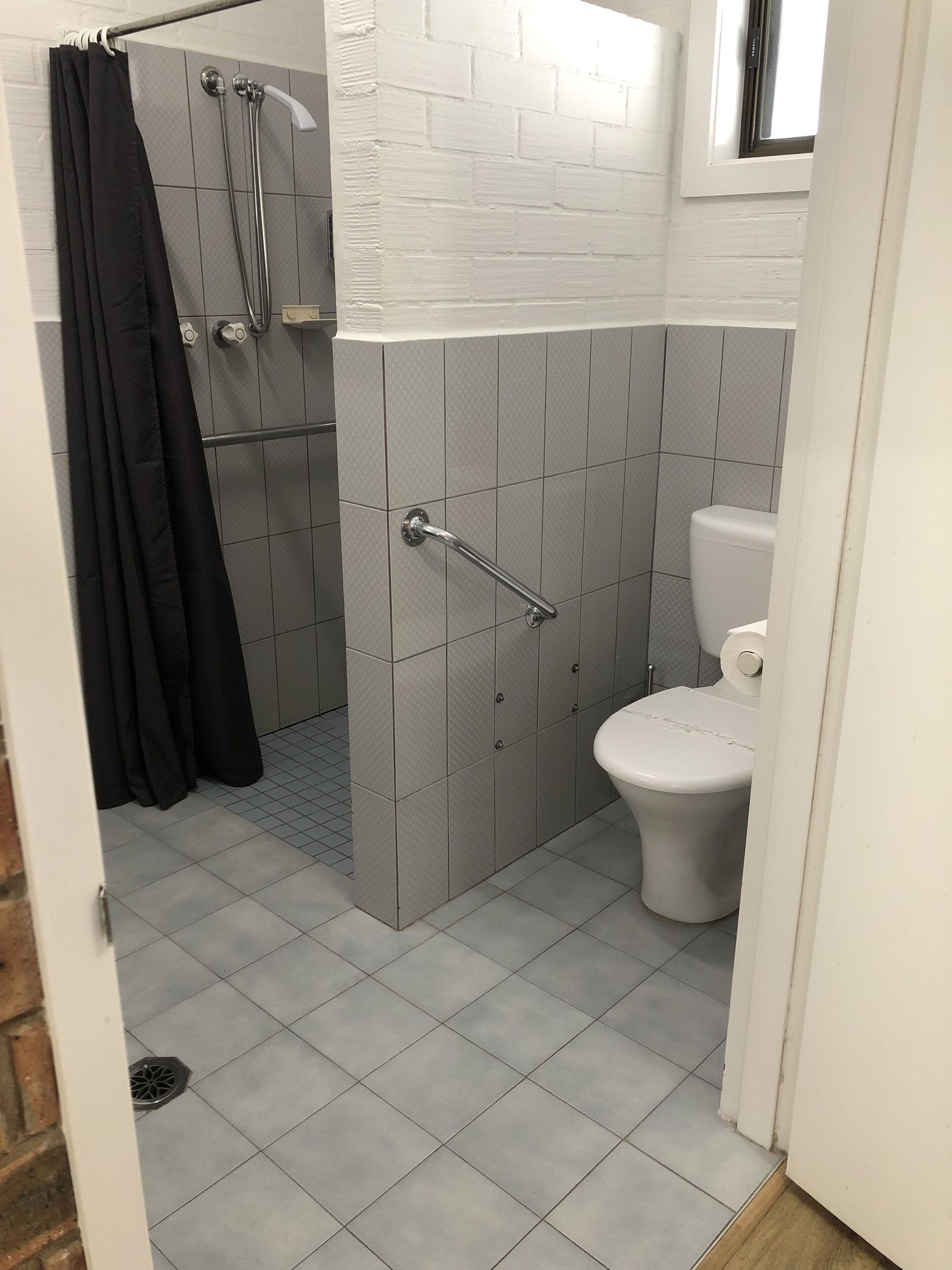 Une salle de bain avec douche, toilettes et carrelage au sol.
