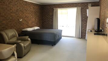 A bedroom with a bed, a leather chair, a desk with a computer, and a brick wall.