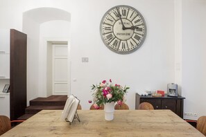 A dining area with a wooden table, a clock, and a vase of flowers.