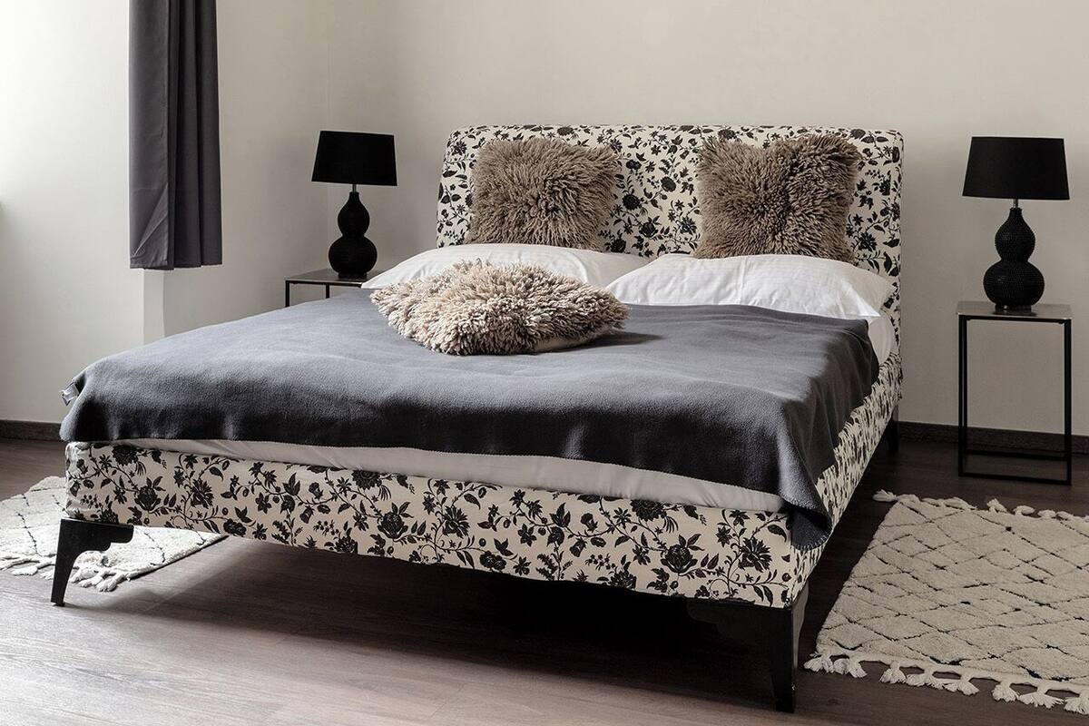 A bedroom with a bed, two bedside tables, a floor lamp, a large window with a curtain, and a rug.
