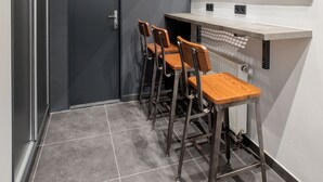 Un corridoio stretto con una porta scura, uno specchio sopra un bancone e tre sedie di legno.