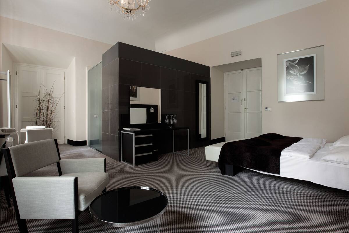 A hotel room with a bed, a desk, a chair, a round table, and a large mirror.