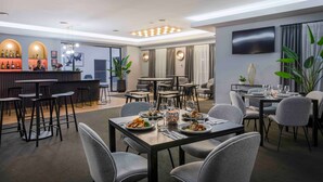 Un comedor moderno con mesas y sillas, una zona de bar con taburetes y un televisor montado en la pared.