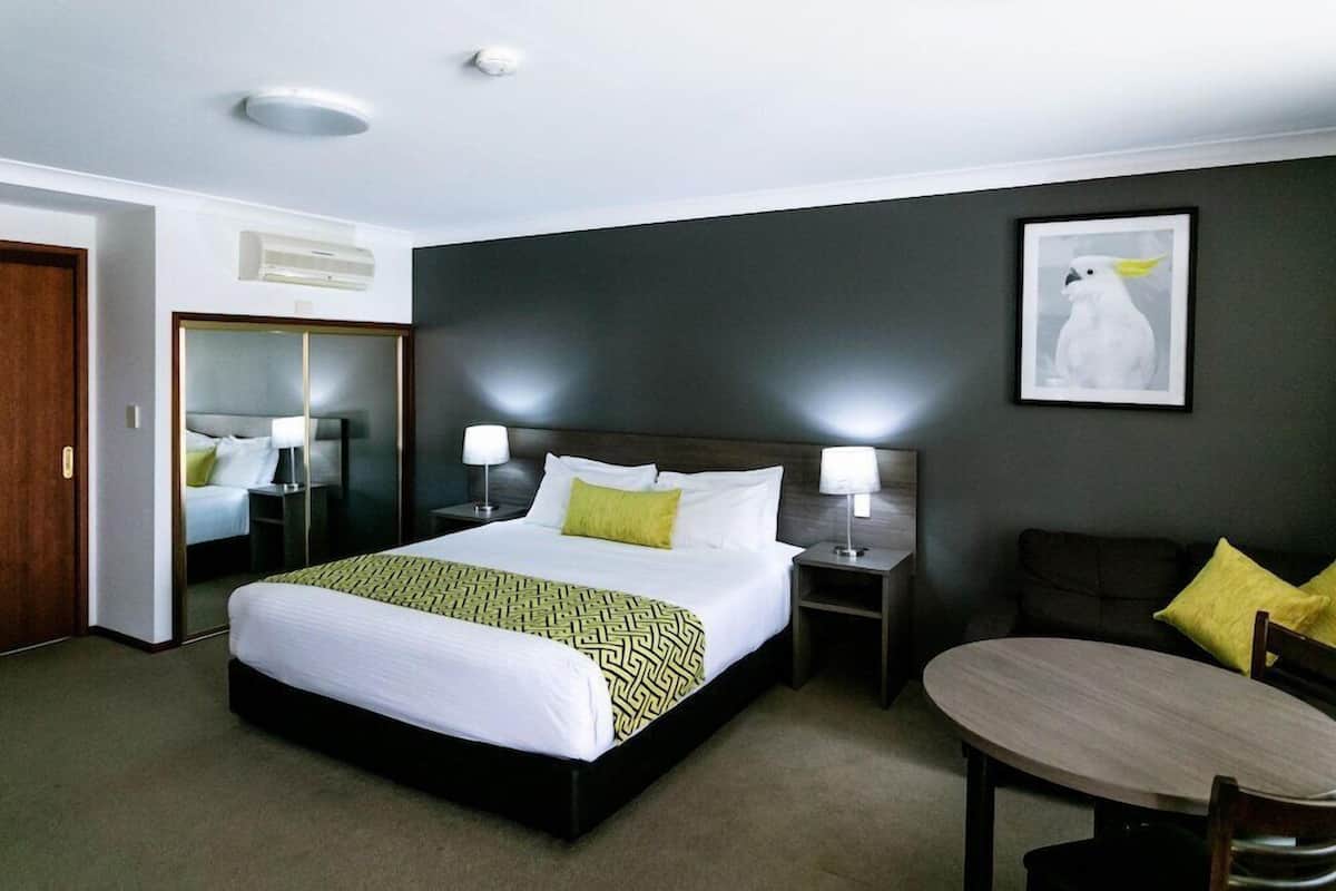 A hotel room with a bed, bedside tables, a chair, a table, a mirror, and a framed picture on the wall.