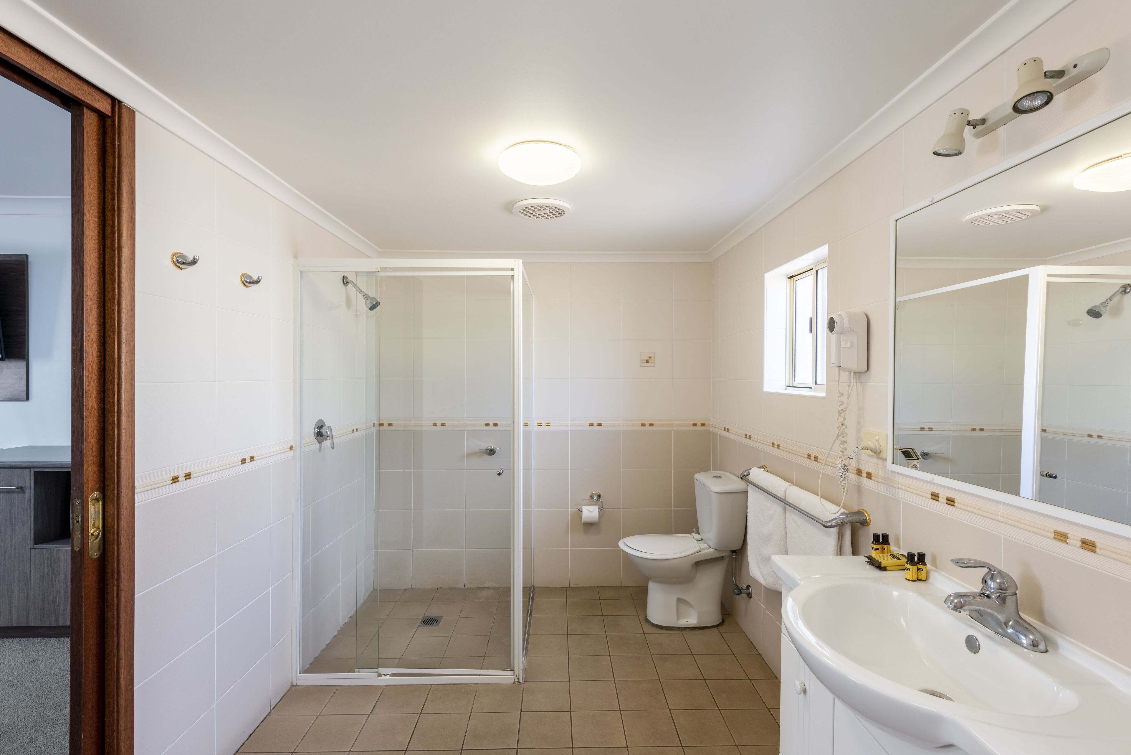 A bathroom with a shower, toilet, sink, and a large mirror.