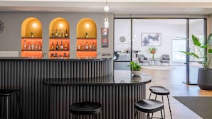 Un área de bar moderna con una barra curva, tres arcos iluminados y una zona de estar con taburetes.