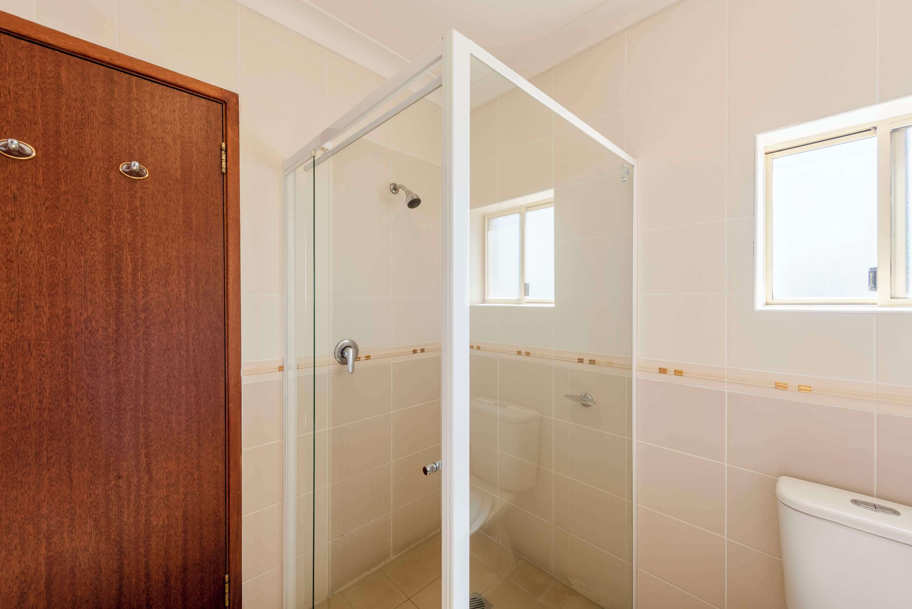 Un baño con ducha envuelta en vidrio, una puerta de madera y un inodoro.