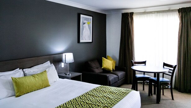 Habitación de hotel con cama, sofá, mesa de comedor con sillas, lámpara y un cuadro en la pared.