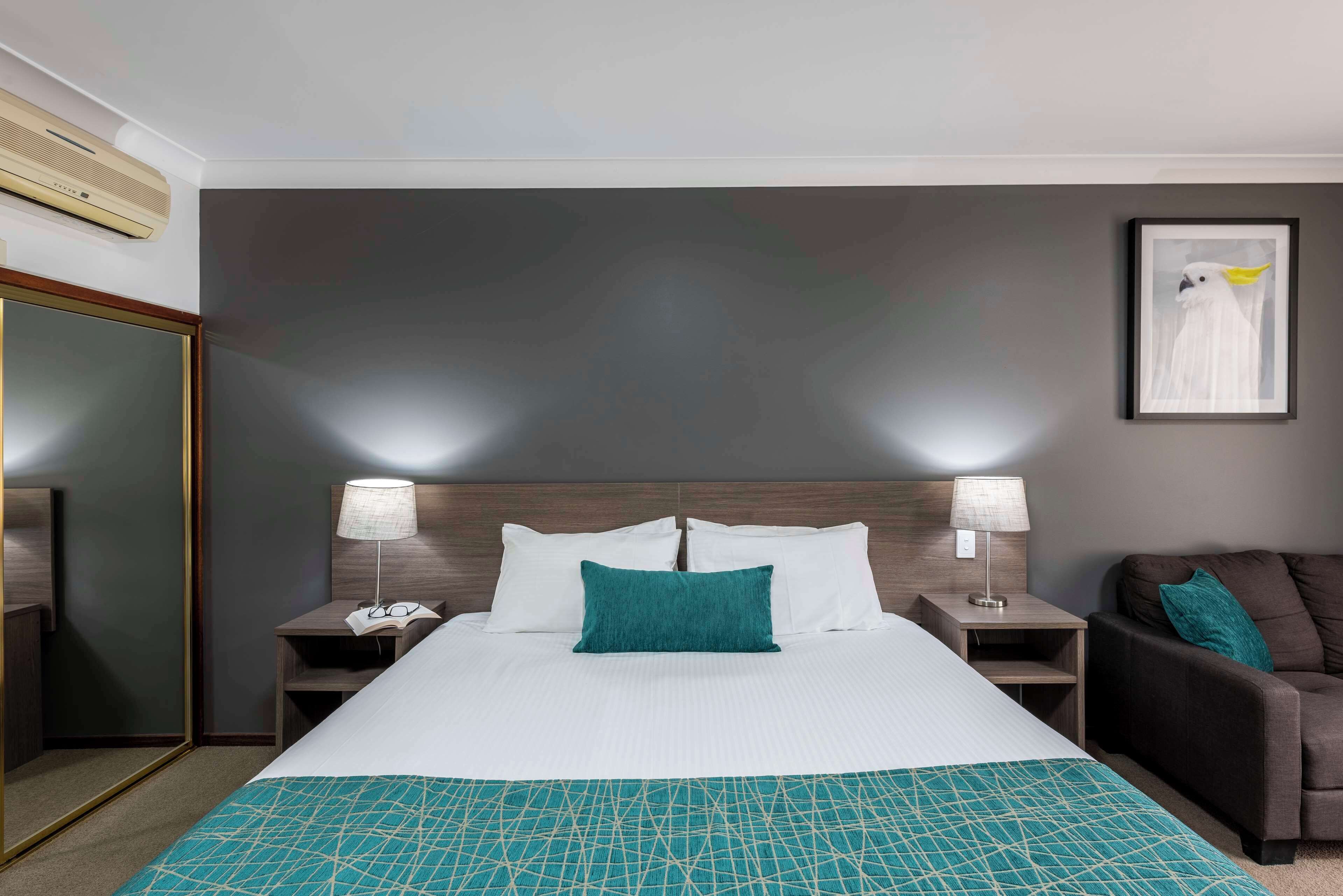 A hotel room with a large bed, two bedside tables with lamps, a nightstand, a couch, and a framed picture on the wall.