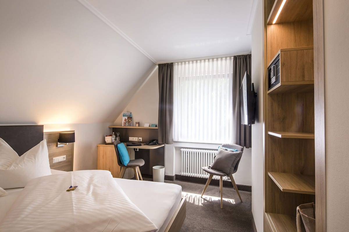 Una habitación de hotel con cama, escritorio, silla, radiador y ventana con cortinas.