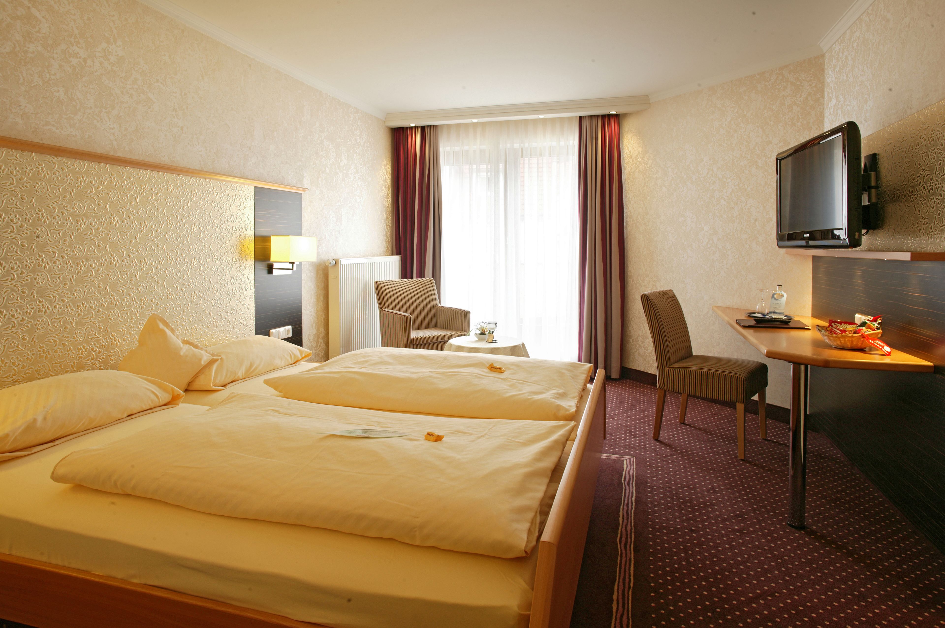 A hotel room with a large bed, a desk with a television, and a chair.