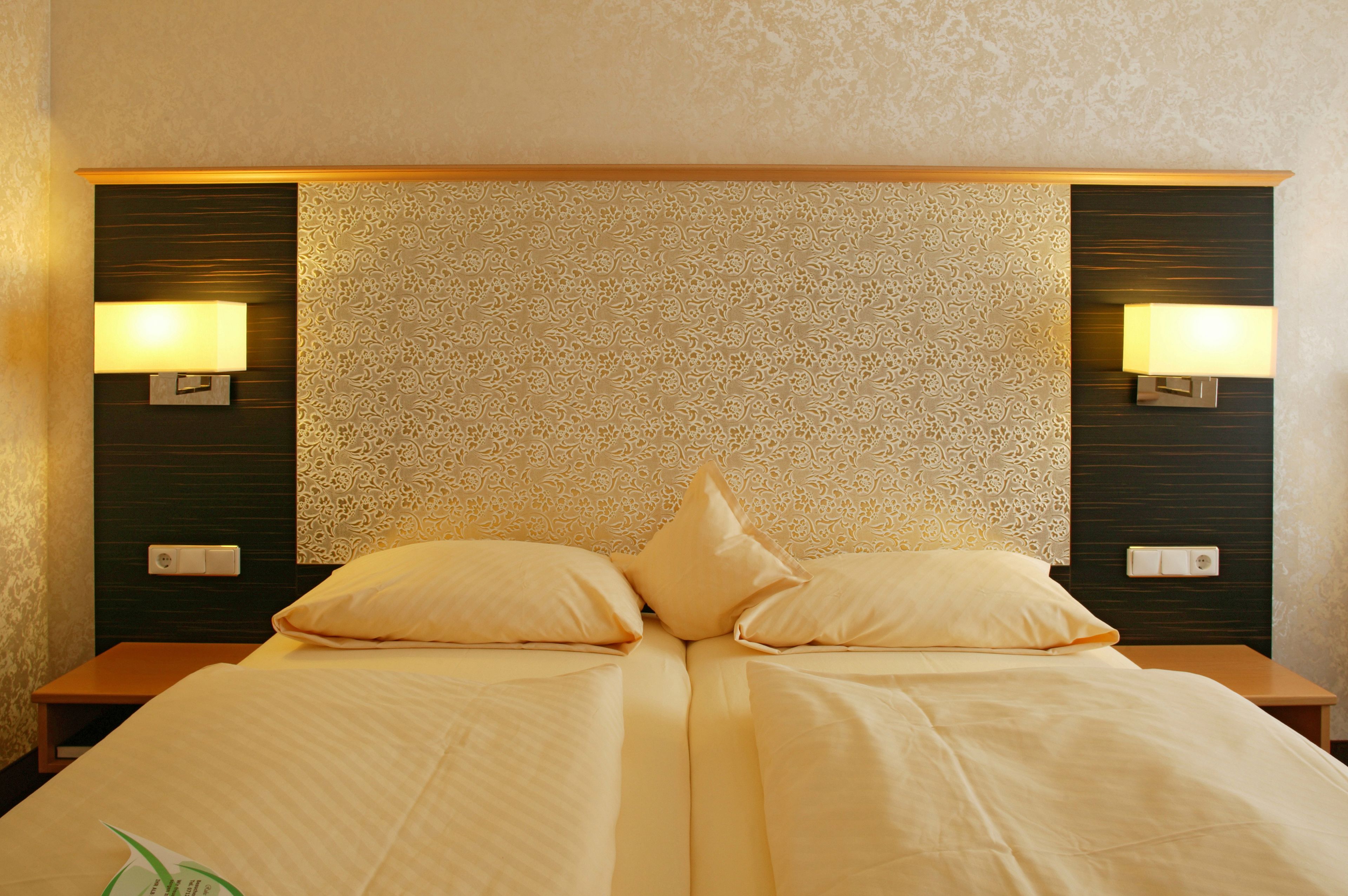 Ein Doppelbett mit zwei Kissen, ein Nachttisch mit Lampe und eine Wand mit einem gemusterten Design.