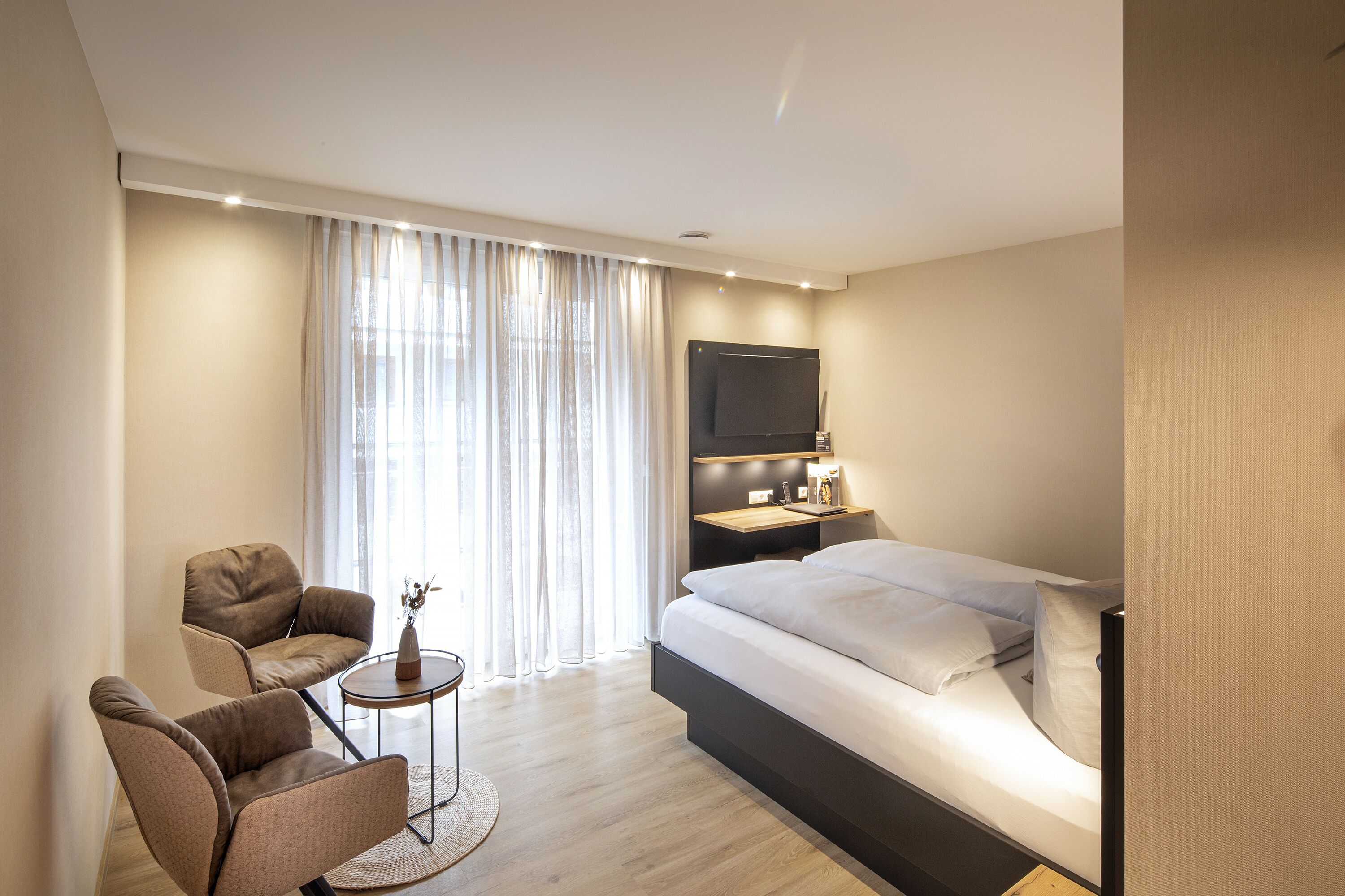 Una habitación de hotel moderna con una cama grande, un escritorio con televisor de pantalla plana, una silla y una pequeña mesa con un florero.
