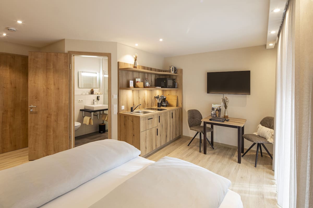 Una habitación de hotel compacta con una cama, una pequeña kitchenette, un escritorio y un televisor.