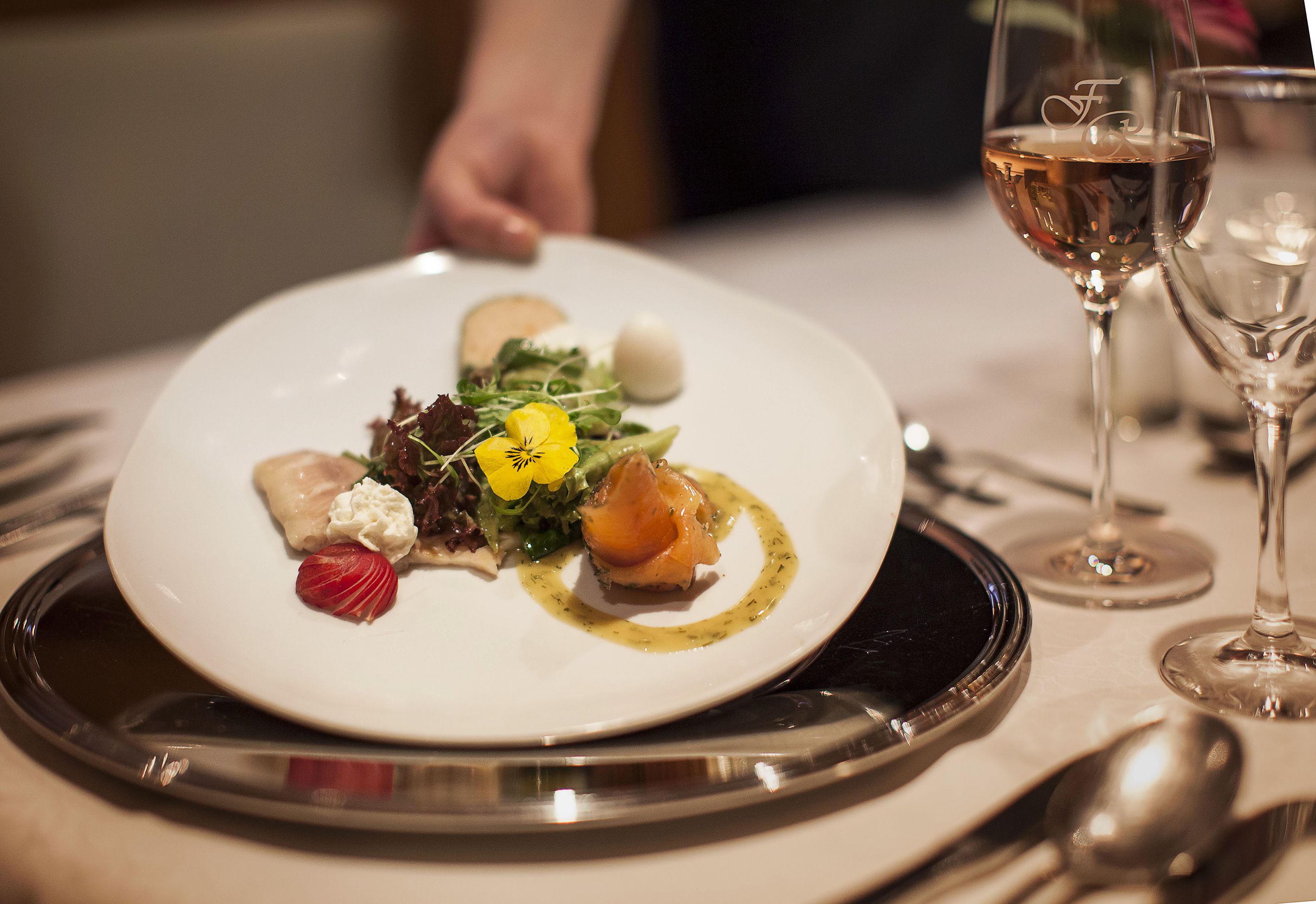 Une assiette blanche avec une salade et un verre de vin sur une table.