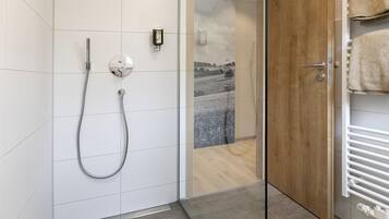 A modern bathroom with a glass shower enclosure, a wooden door, and a towel rack.