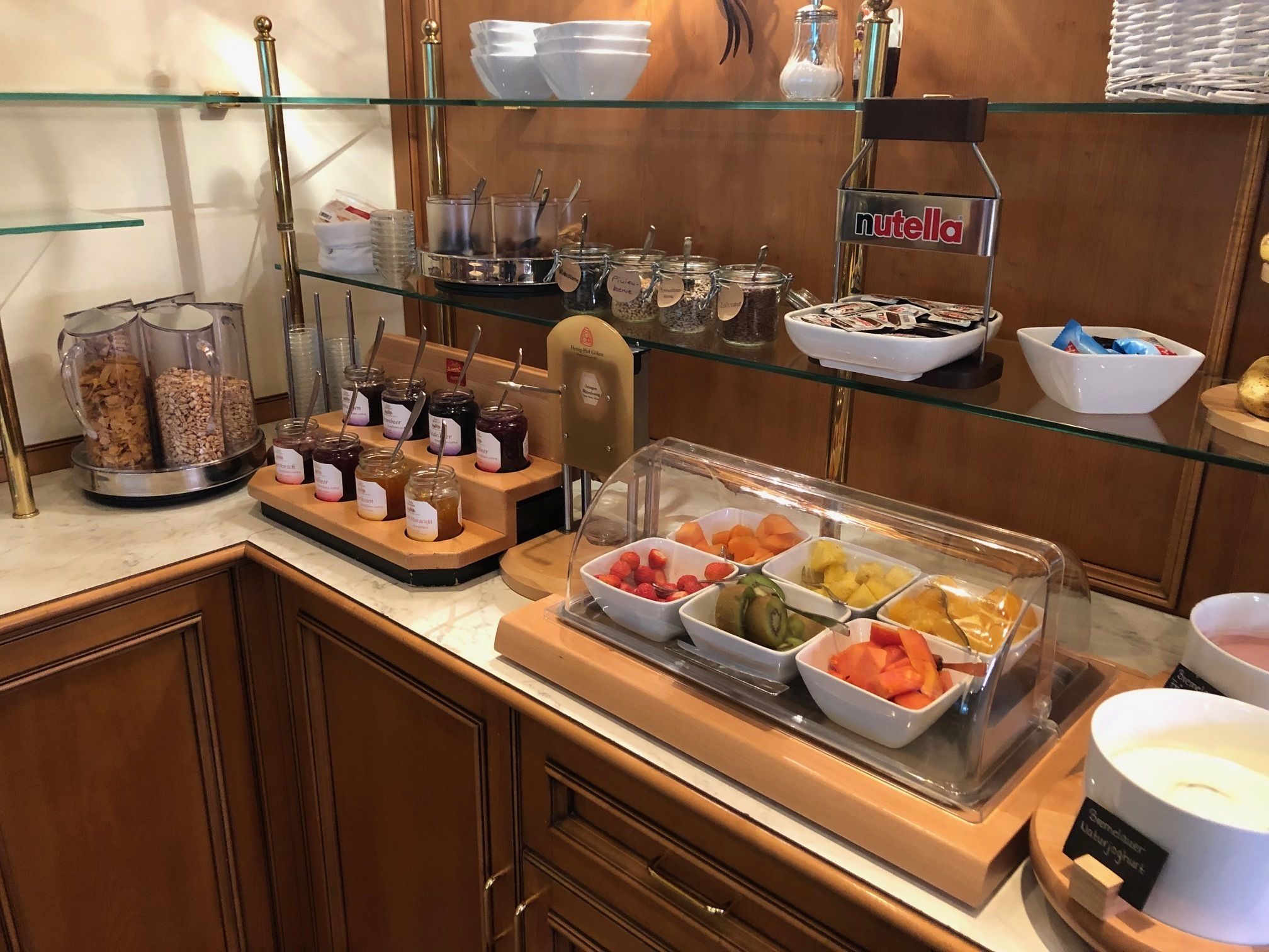 Un bufé con diversos alimentos, incluyendo frascos de pastas, tazones de frutas y un dispensador de Nutella.