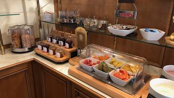 Un bufé con diversos alimentos, incluyendo frascos de pastas, tazones de frutas y un dispensador de Nutella.