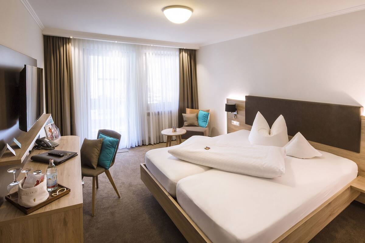 Habitación de hotel con una cama grande, un escritorio con computadora y una silla, una mesita redonda y un televisor.