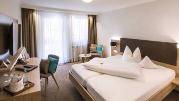 A hotel room with a large bed, a desk with a computer and a chair, a small round table, and a TV.