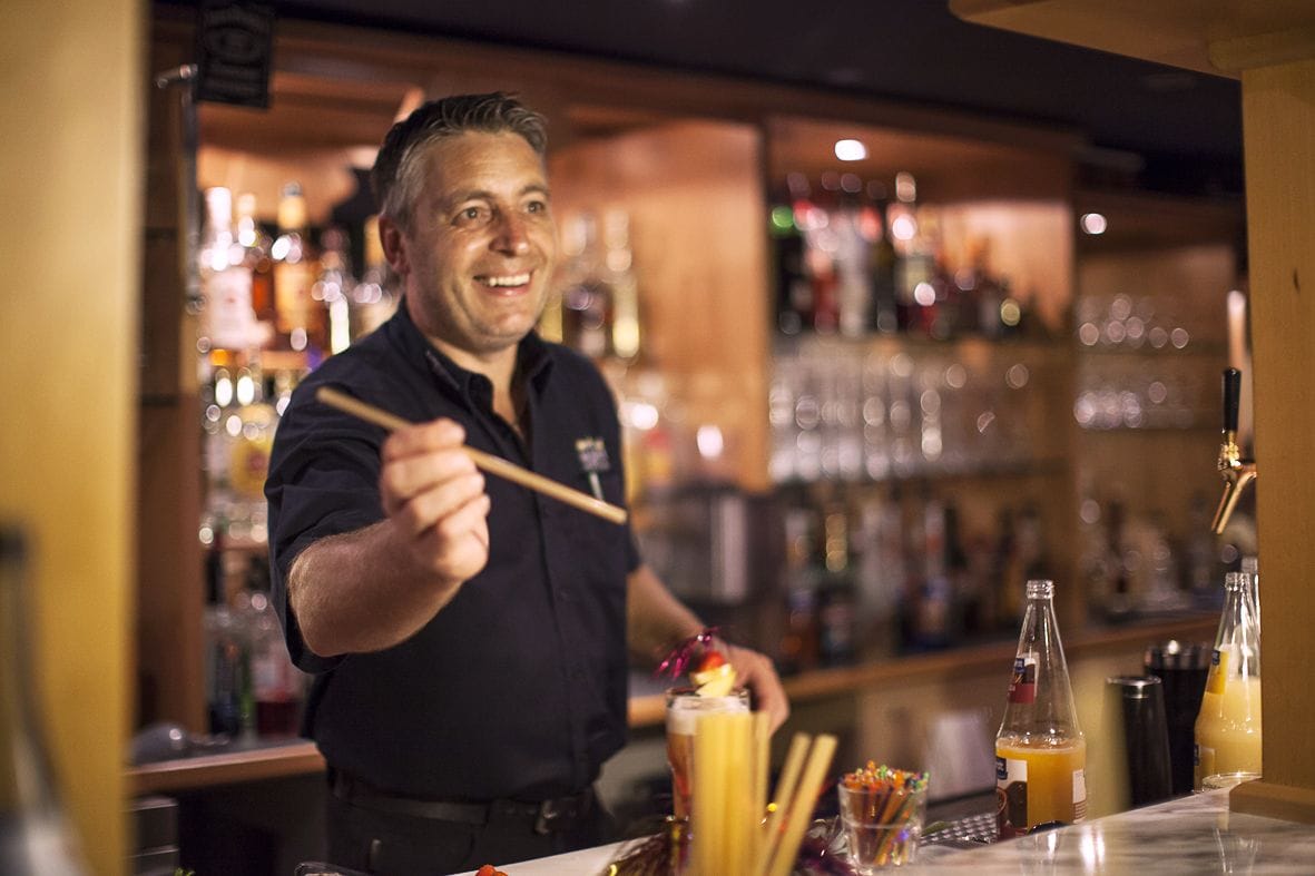 Un barman derrière un comptoir, avec une variété de bouteilles et de verres en arrière-plan.