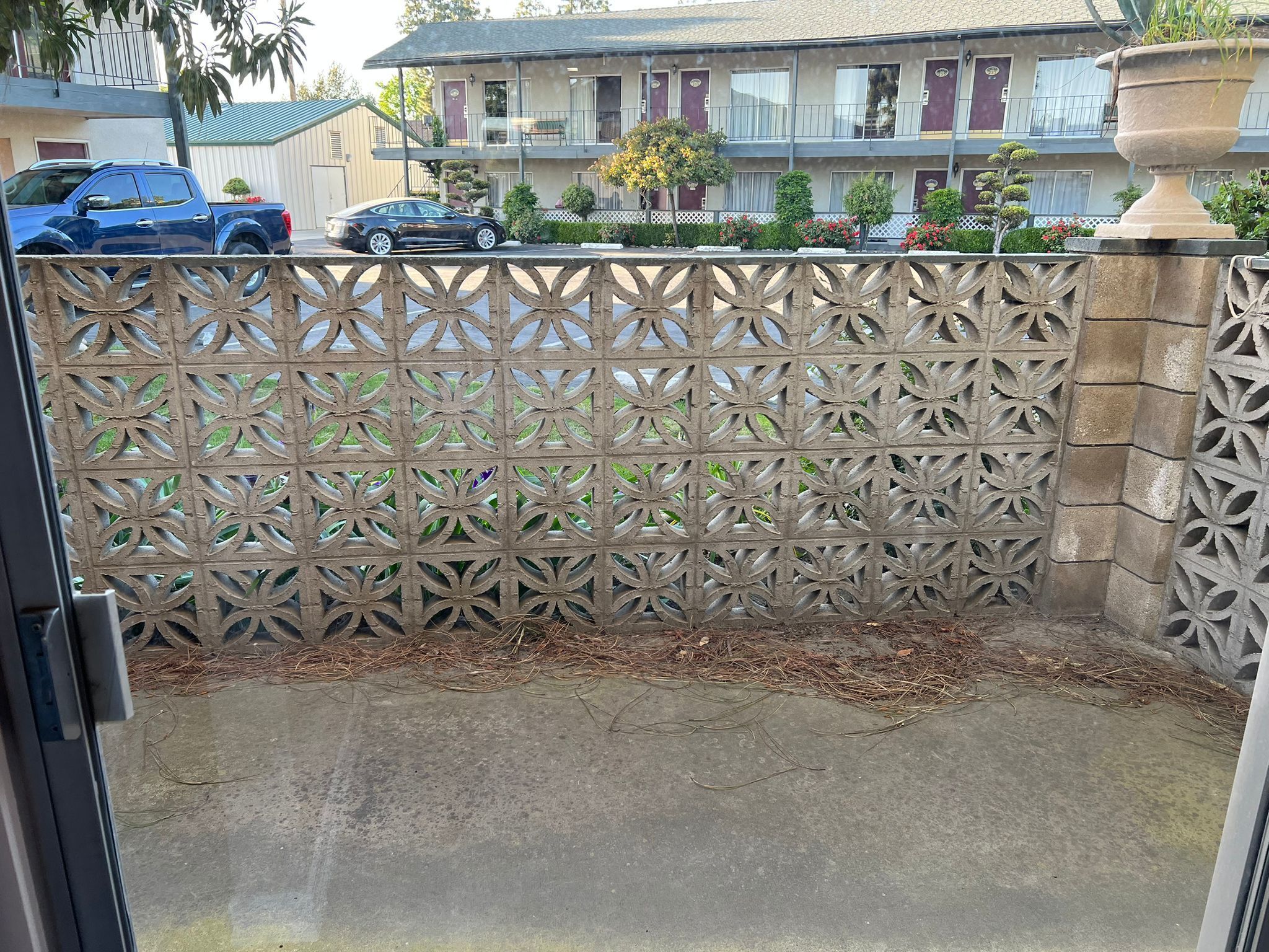A view through a decorative metal fence with a concrete base, leading to a residential area with houses and parked cars.