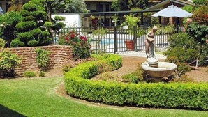 A well-maintained garden with a statue, a swimming pool, and a stone wall.