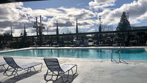 A swimming pool with lounge chairs, a fence, and street lamps.