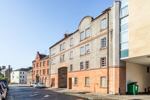 Una calle adoquinada con edificios históricos, un contenedor verde y coches aparcados.