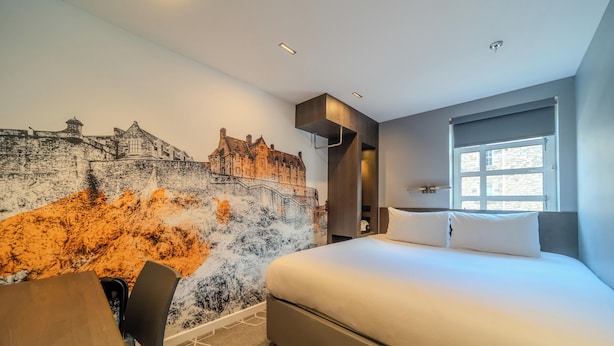 A modern hotel room with a large bed, a dining table, and a mural of a castle. - KM Hotel (Edinburgh)