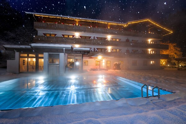 A hotel with a swimming pool surrounded by snow, illuminated by warm lights, and featuring multiple balconies with lights. - Landhof Ellmau (Ellmau)