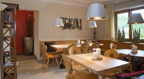 A dining area with wooden tables and chairs, a bench, and a wall-mounted painting. - Landhof Ellmau (Ellmau)