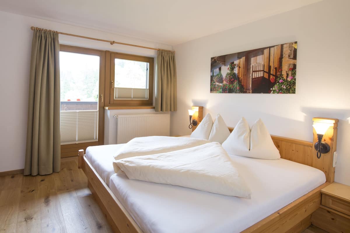 Un dormitorio con una cama de madera, dos mesitas de noche con lámparas, una ventana con cortinas y un cuadro en la pared.