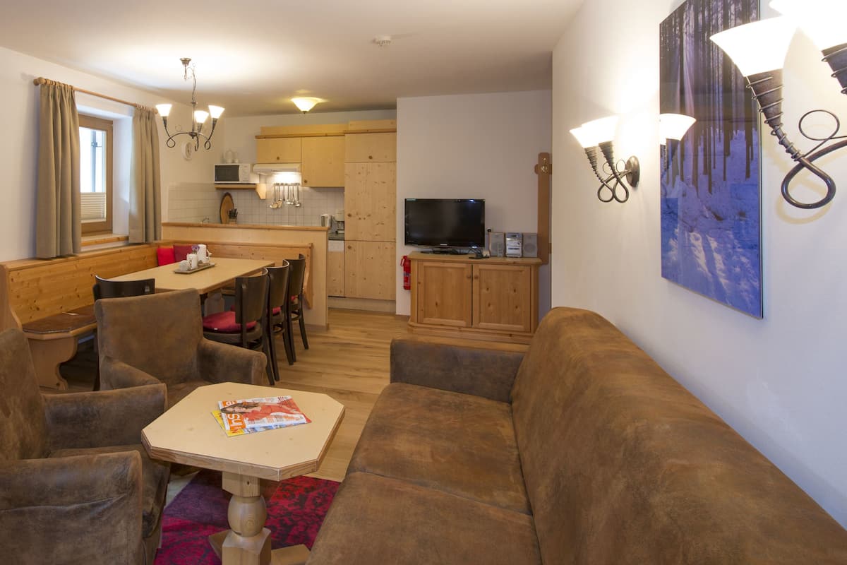 Una sala de estar acogedora con sofá, sillones, una mesita y una cocina al fondo.