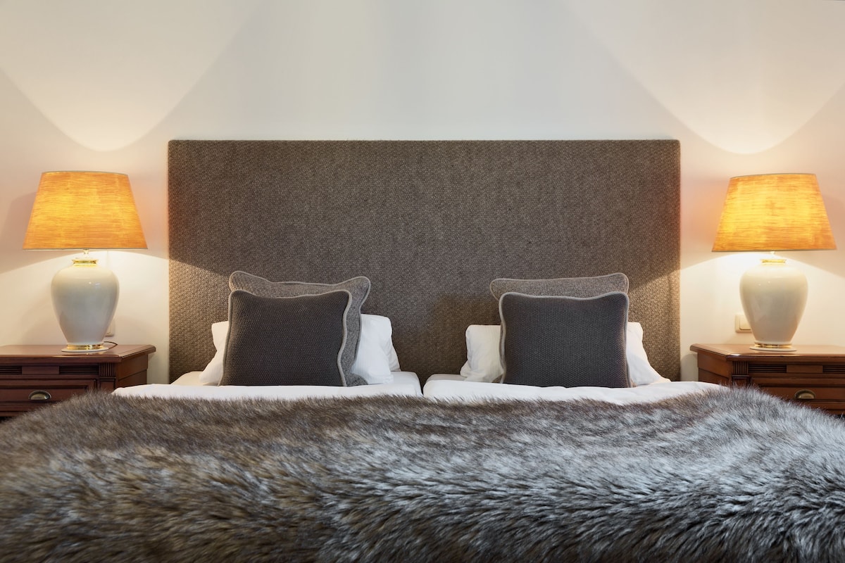 Habitación de hotel con una cama grande, dos mesitas de noche, dos lámparas y un cabecero con textura.