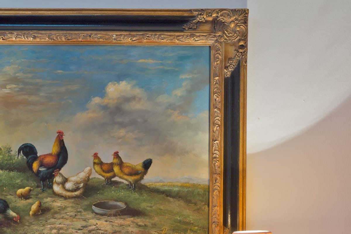 Una pintura de gallinas, una mesa con manzanas y una lámpara.