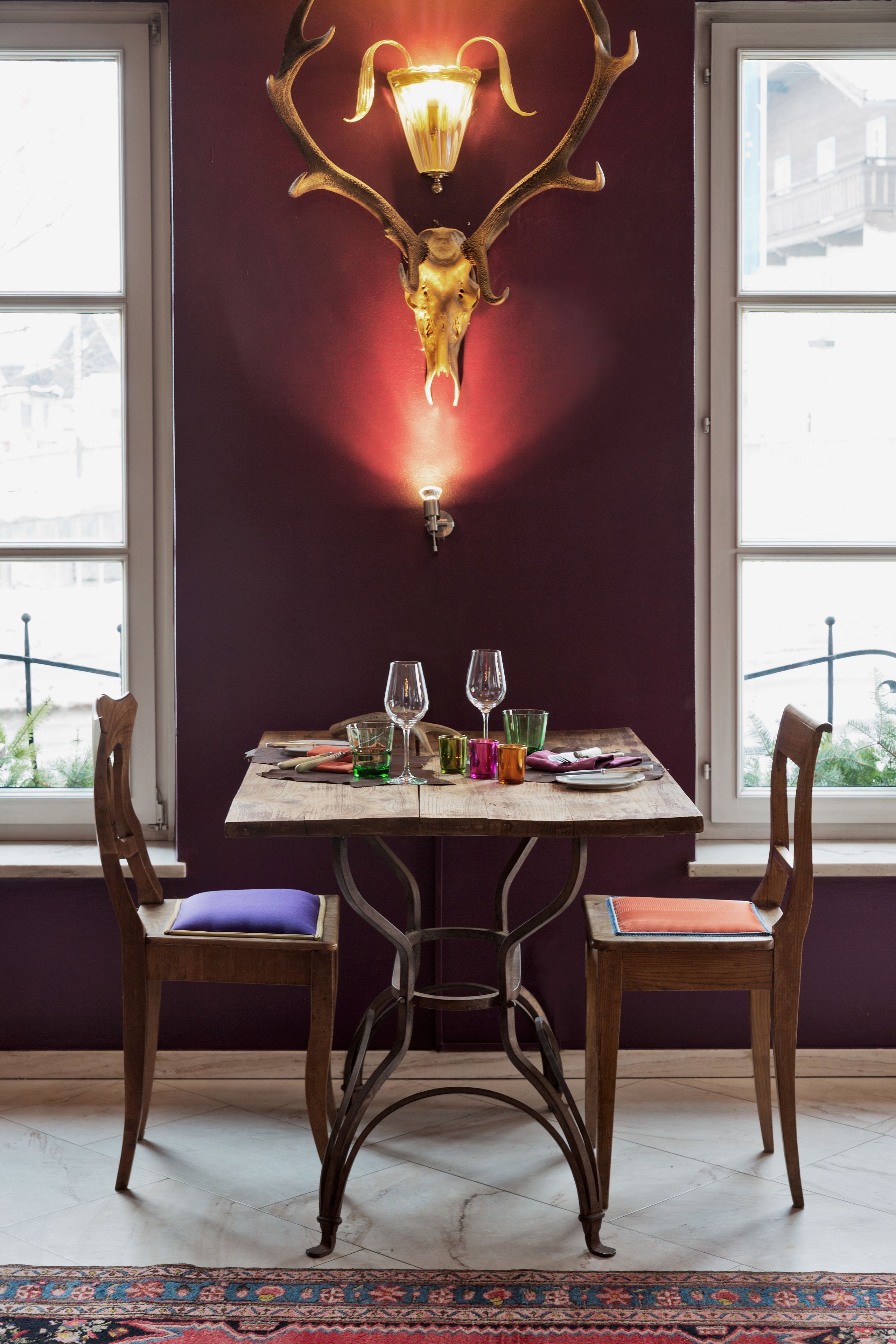 Un coin repas avec une table dressée pour deux personnes, un luminaire décoratif fixé au mur et une vue par la fenêtre.