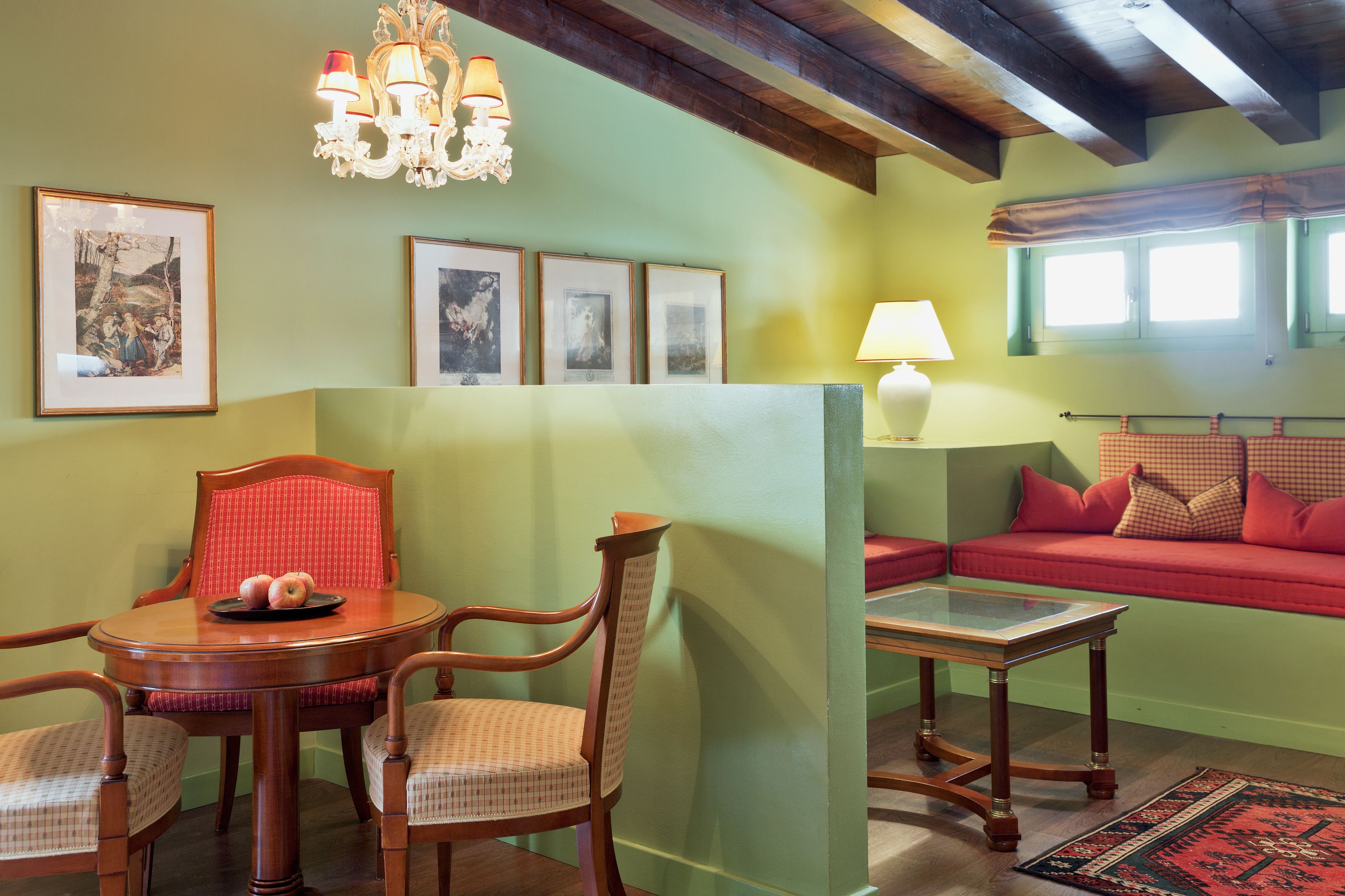 A room with a dining table and chairs, a sofa, a chandelier, and framed pictures on the wall.