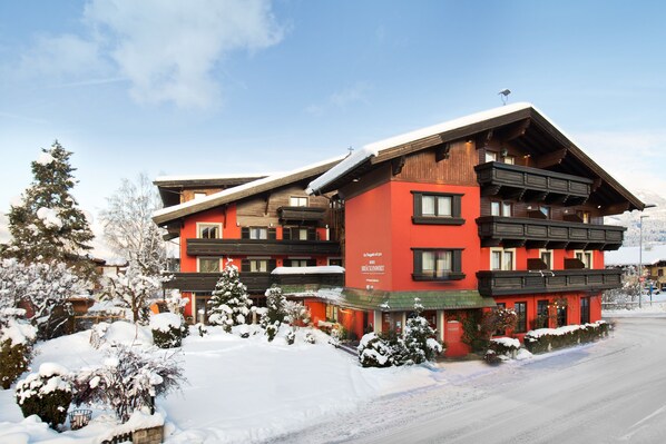 A red and black chalet-style building with multiple balconies and a ski lift on the roof. - Hotel Bruggwirt (Sankt Johann in Tirol)