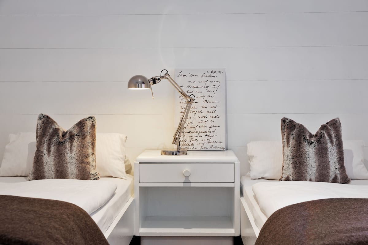 Un dormitorio ordenado con dos camas, una mesita de noche con lámpara y un papel colocado en la pared.