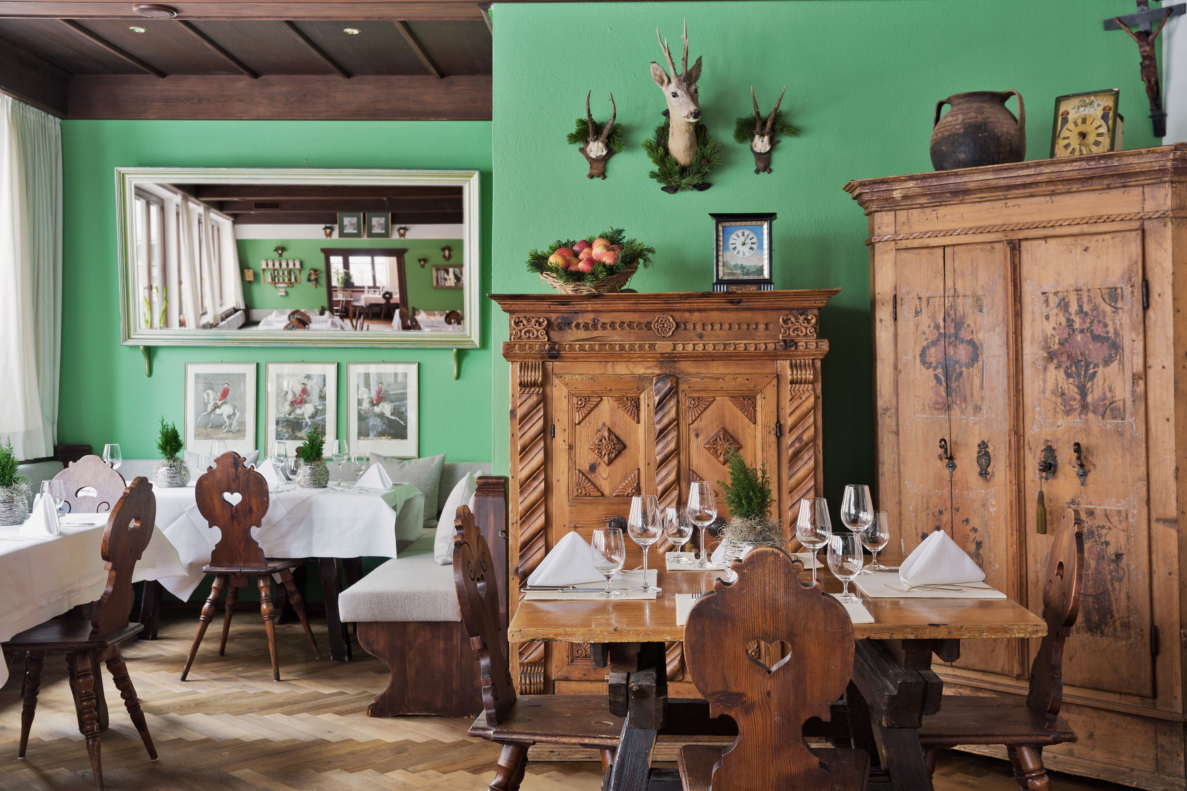 A dining area with wooden tables set for a meal, a green wall with decorative antlers, and a wooden cabinet.