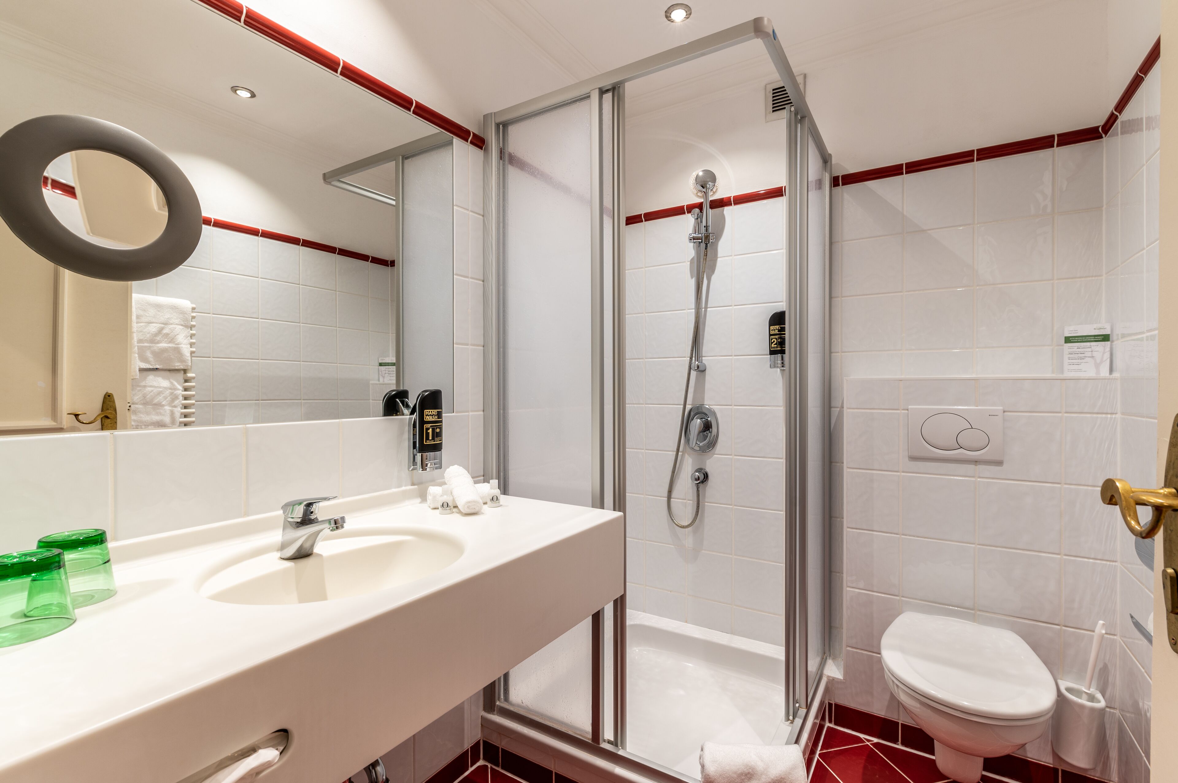 Un baño moderno con ducha de vidrio, lavamanos blanco con espejo y un inodoro.