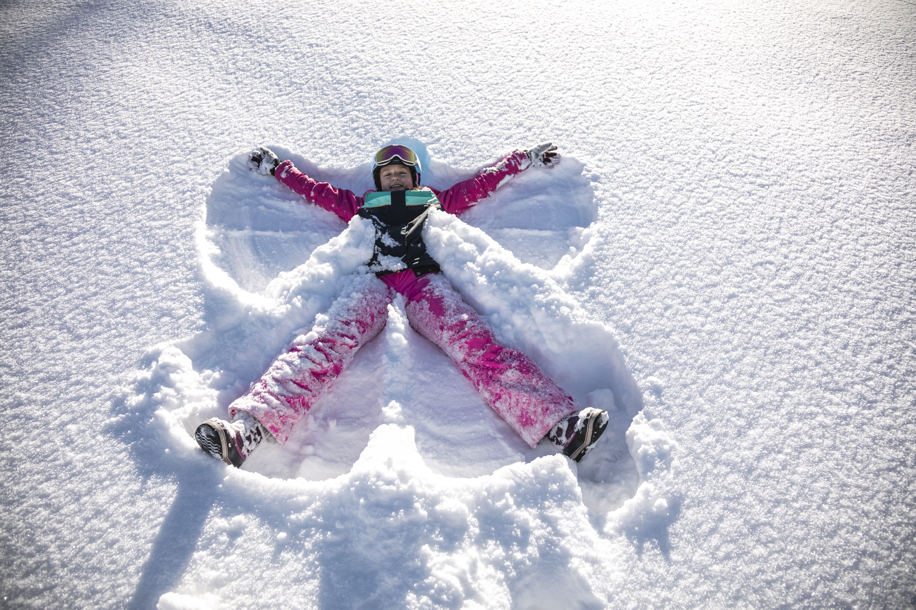 A person lying in a snow angel position on a snowy surface.
