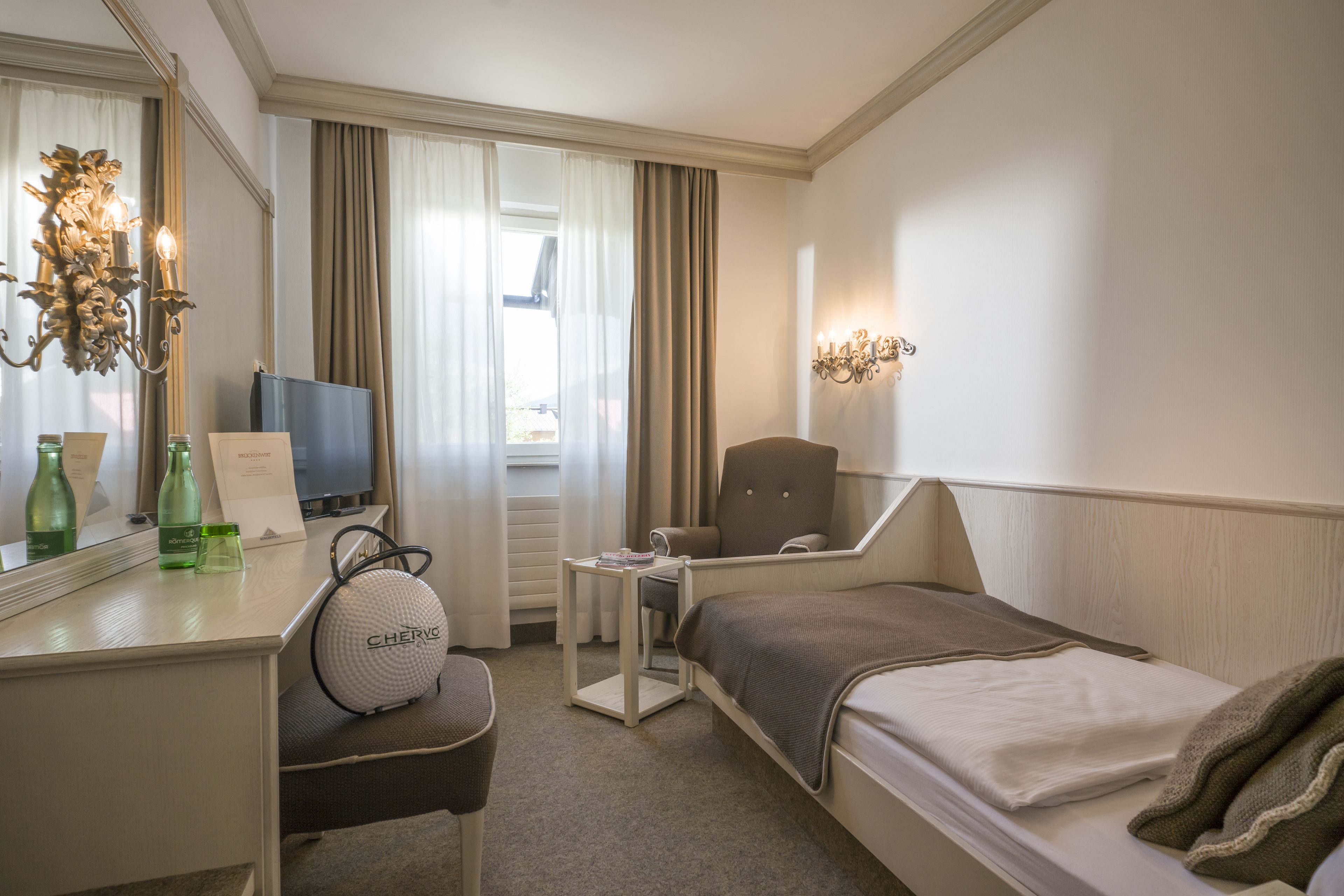 A hotel room with a bed, a desk with a computer, a chair, a TV, and a mirror.