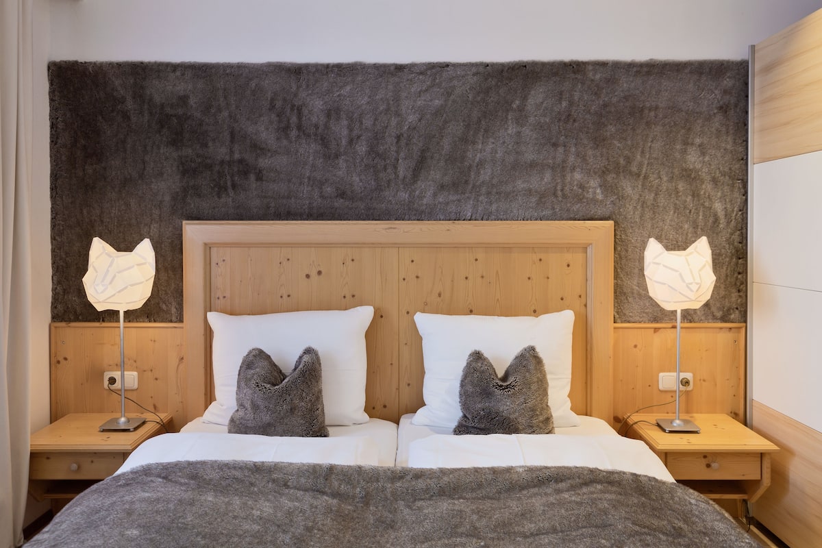 Una cama doble con dos mesitas de noche, cada una con una lámpara. El cabecero es de madera con textura similar al pelaje.
