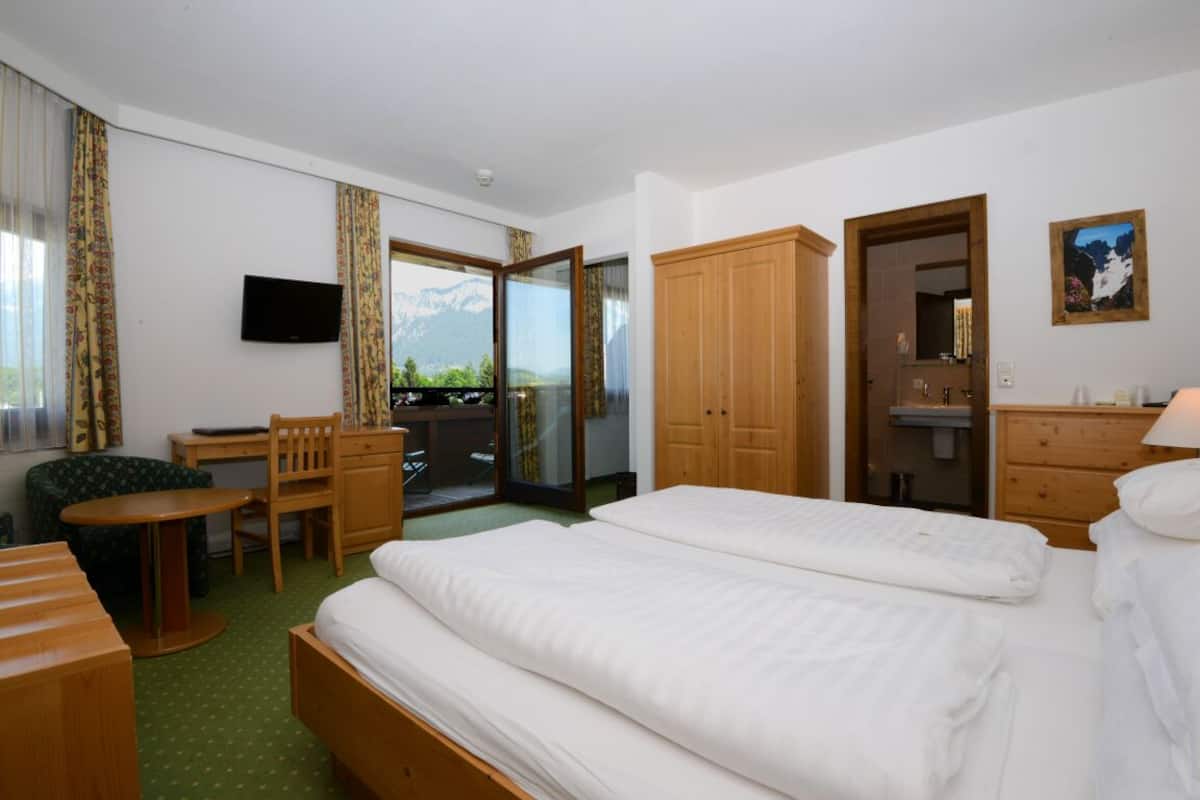 A hotel room with a bed, a desk, a chair, a TV, and a view of mountains.